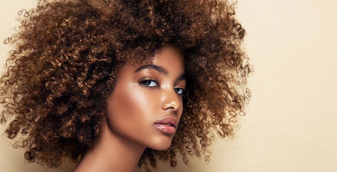 Mulher de pele negra e cabelo cacheados com tom loiro escuro